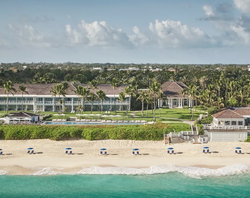 Beachfront resort with palm trees and lounge chairs by turquoise water.