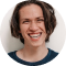 Smiling young person with curly hair and a blue shirt.