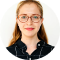 Smiling woman with glasses and long hair wearing a dark blouse.