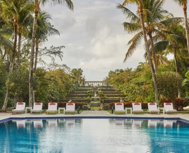 Serene poolside view with palm trees and lounge chairs under a cloudy sky.