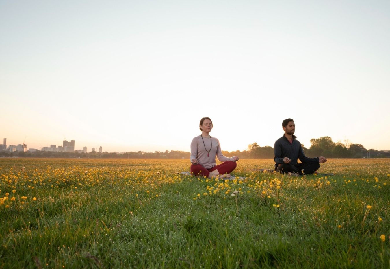 Two people meditating outdoors in a grassy field during sunset.