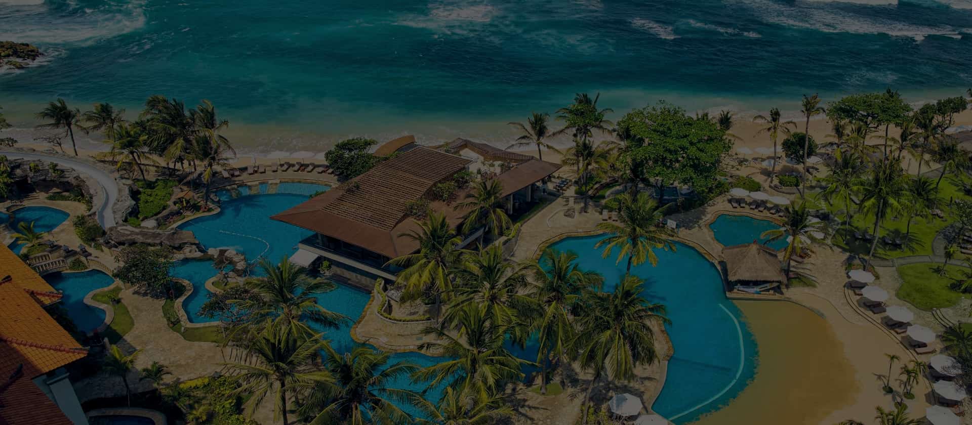 A tropical resort with palm trees and a large pool near the ocean.
