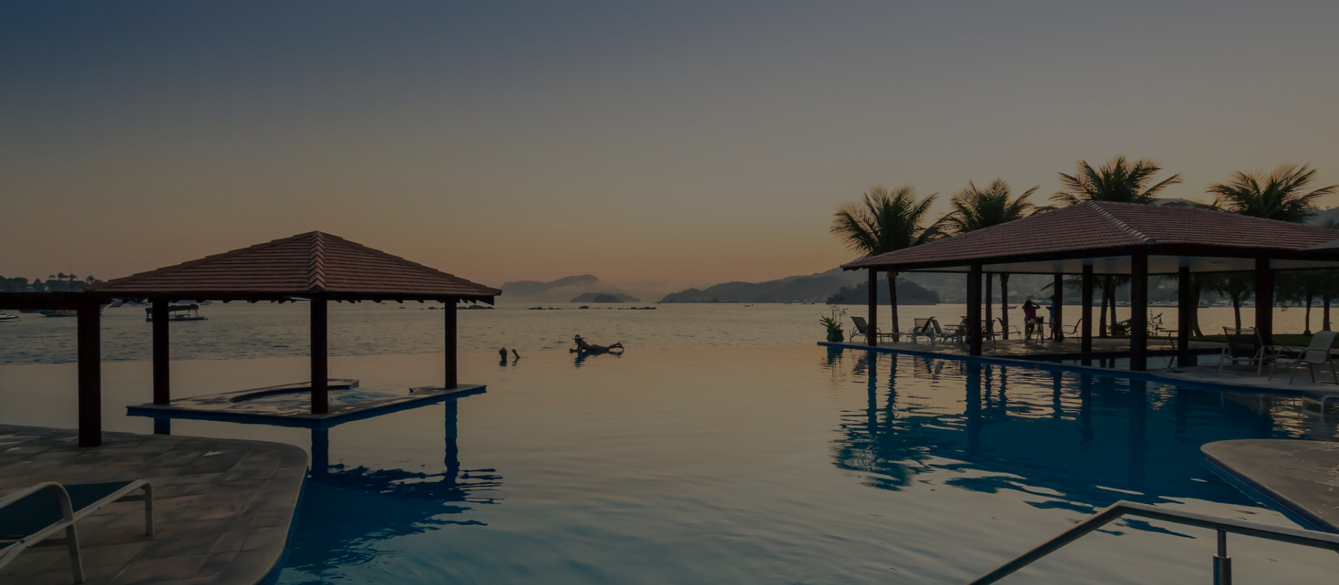 A tranquil infinity pool overlooking a calm sea at sunset with distant islands.