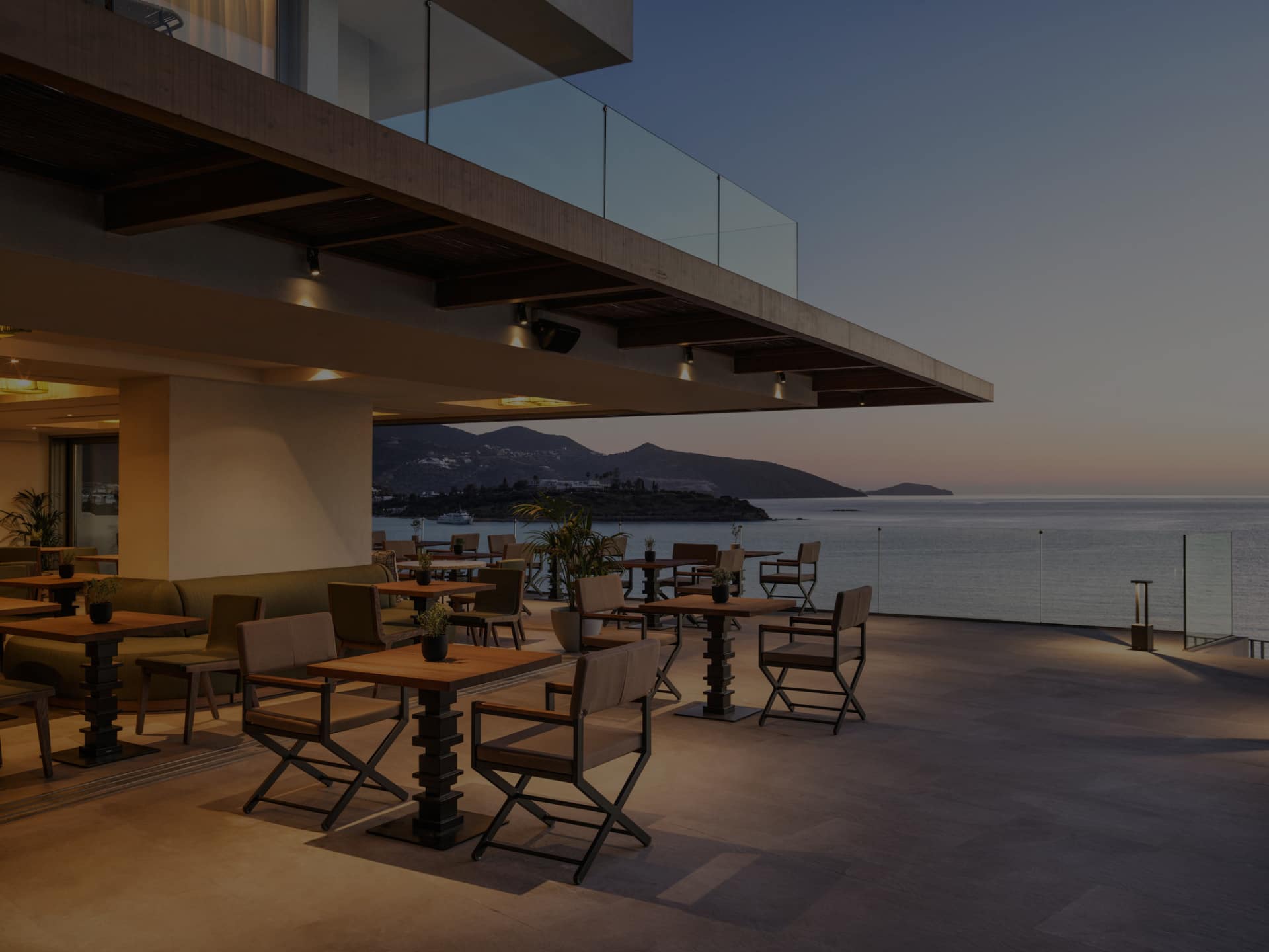 Modern outdoor dining area overlooking a serene waterfront at dusk.